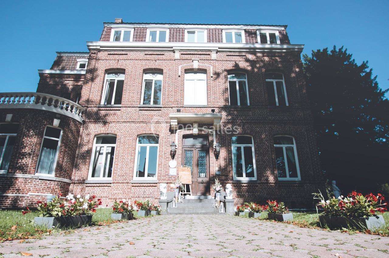 Façade d'une grande maison en briques rouges avec allée pavée et parterres de fleurs au premier plan.