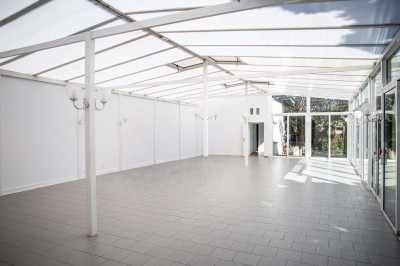 Salle de réception lumineuse avec tables dressées, lustres suspendus et nappes blanches sur des tables latérales.