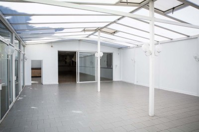 Salle de réception lumineuse avec tables dressées, lustres suspendus et nappes blanches sur des tables latérales.
