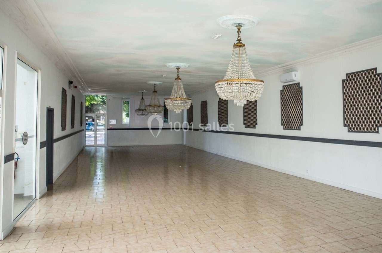 Salle vide avec sol carrelé, murs blancs ornés de panneaux décoratifs et lustres suspendus au plafond.