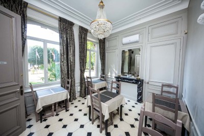 Salle de réception lumineuse avec tables dressées, lustres suspendus et nappes blanches sur des tables latérales.