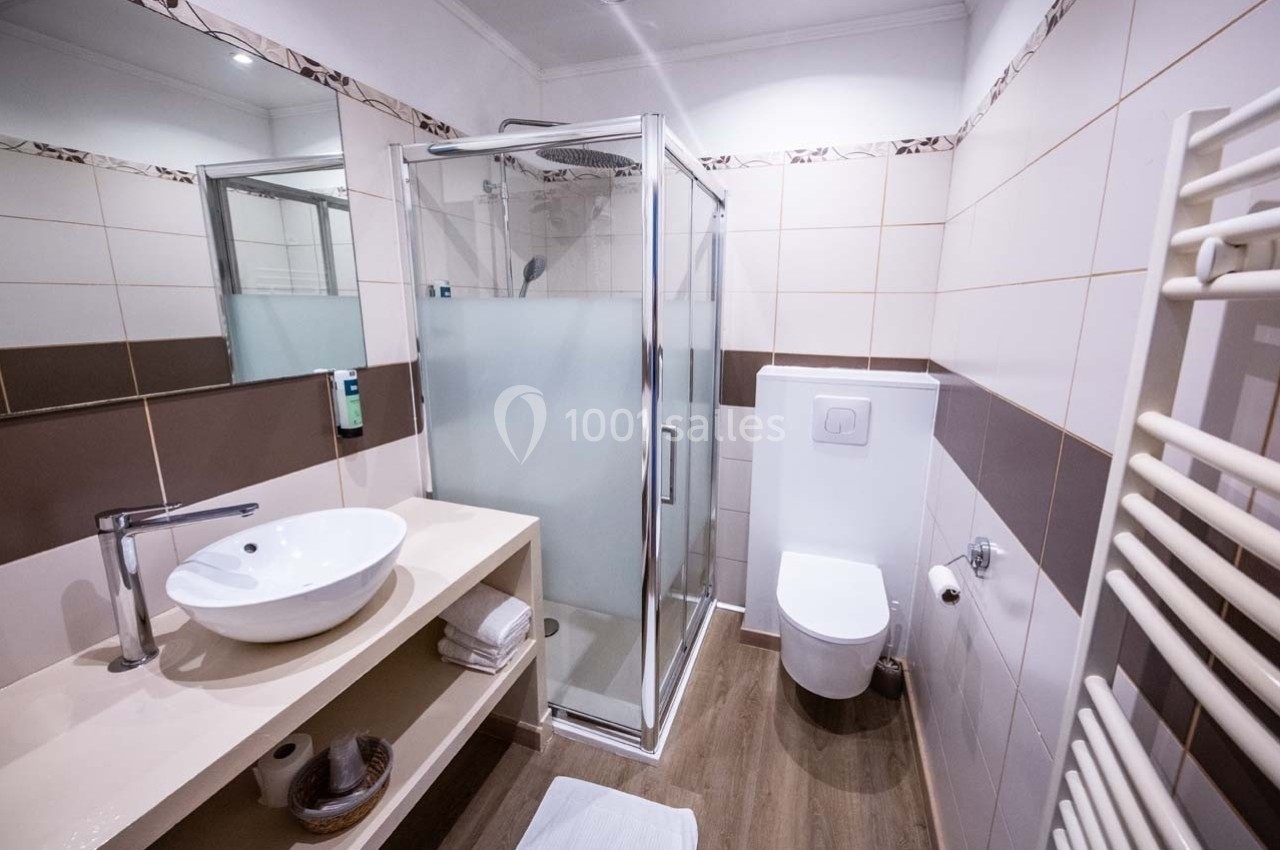 Salle de bain moderne avec douche vitrée, lavabo sur meuble beige, toilettes suspendues et carrelage mural.