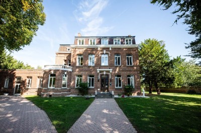 Salle de réception lumineuse avec tables dressées, lustres suspendus et nappes blanches sur des tables latérales.