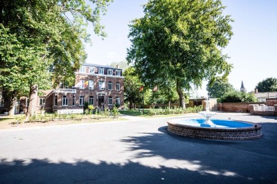 Salle de réception lumineuse avec tables dressées, lustres suspendus et nappes blanches sur des tables latérales.