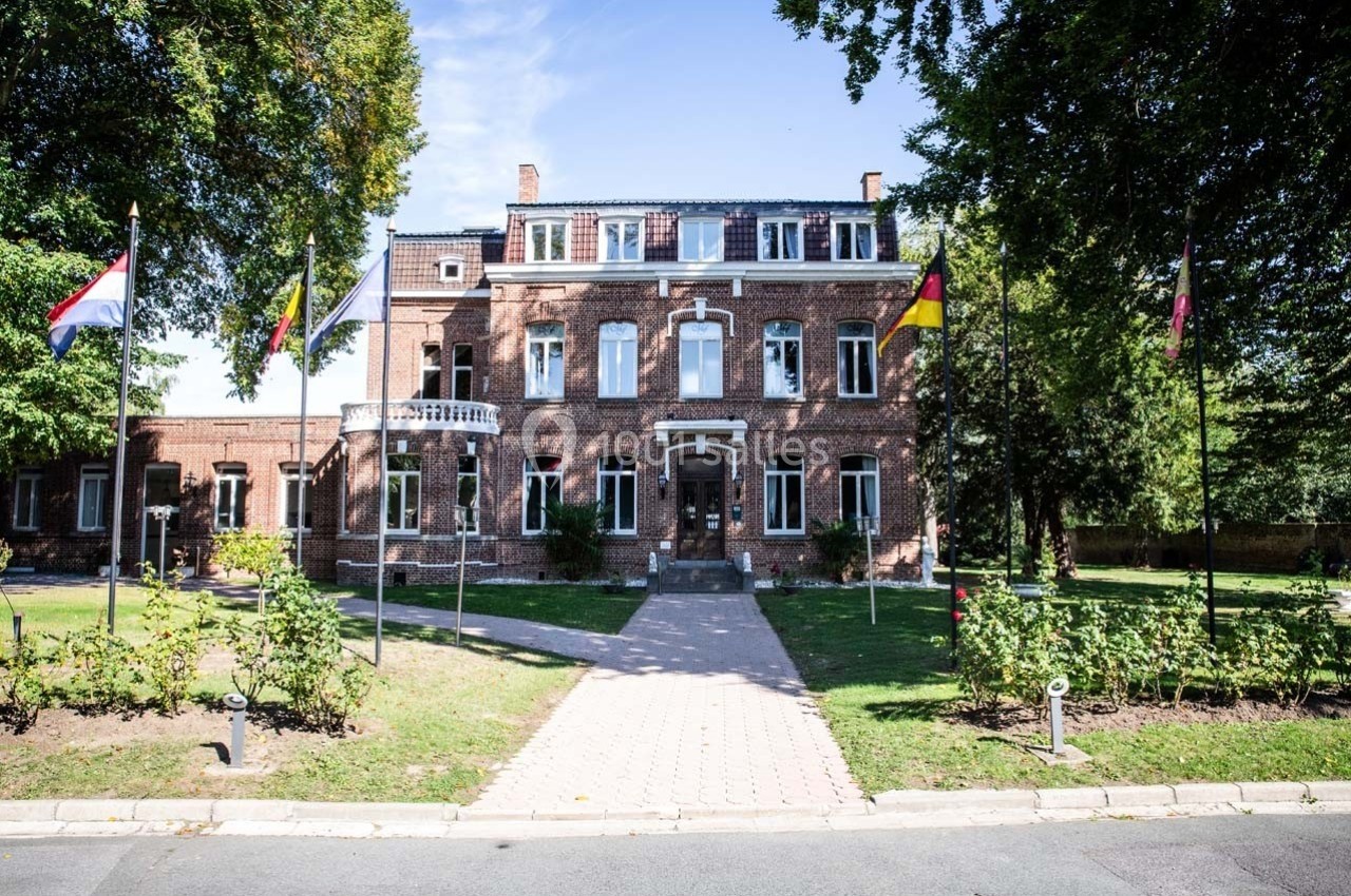 Bâtiment en briques rouges entouré de jardins, avec des drapeaux nationaux alignés sur le devant.