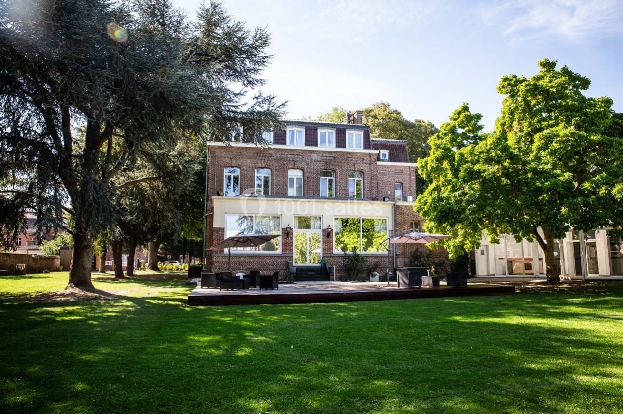 Façade d'un bâtiment en briques entouré d'arbres et donnant sur une pelouse verdoyante par une journée ensoleillée.
