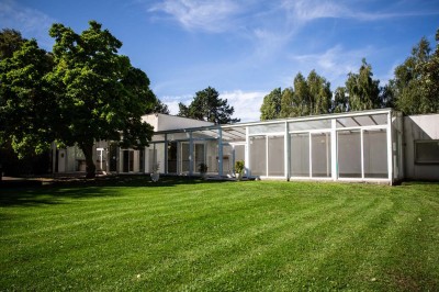 Salle de réception lumineuse avec tables dressées, lustres suspendus et nappes blanches sur des tables latérales.