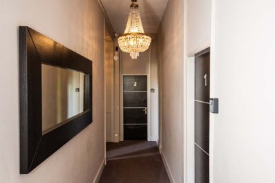 Salle de réception lumineuse avec tables dressées, lustres suspendus et nappes blanches sur des tables latérales.