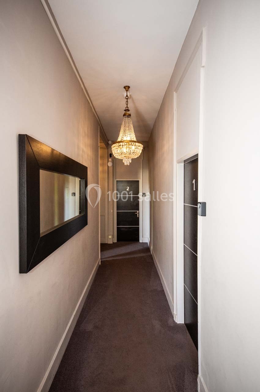 Couloir étroit avec moquette, miroir mural, lustre suspendu et portes numérotées 1 et 2 au fond.