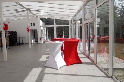 Salle de réception lumineuse avec tables dressées, lustres suspendus et nappes blanches sur des tables latérales.