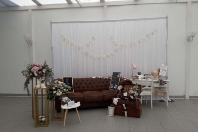 Salle de réception lumineuse avec tables dressées, lustres suspendus et nappes blanches sur des tables latérales.