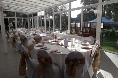 Salle de réception lumineuse avec tables dressées, lustres suspendus et nappes blanches sur des tables latérales.