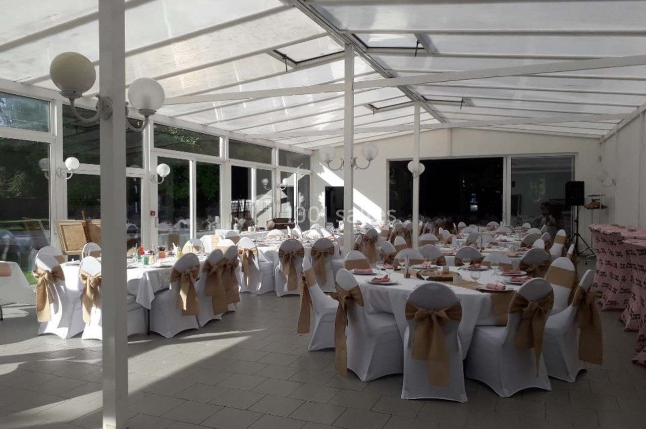 Salle de réception lumineuse avec des tables rondes dressées, chaises blanches décorées de nœuds beiges.