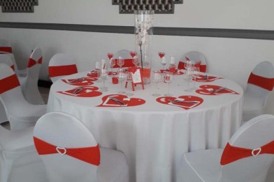 Salle de réception lumineuse avec tables dressées, lustres suspendus et nappes blanches sur des tables latérales.