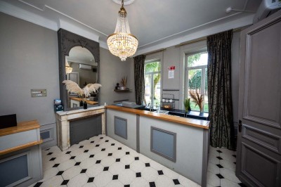 Entrée élégante avec un sol en mosaïque, un lustre en cristal, deux vases décoratifs et une statue en bois.