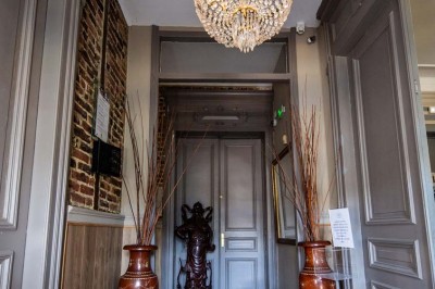 Entrée élégante avec un sol en mosaïque, un lustre en cristal, deux vases décoratifs et une statue en bois.