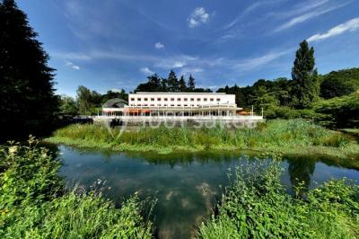 Salle lumineuse avec une grande table dressée pour un repas, décorée de fleurs et entourée de baies vitrées donnant sur un…