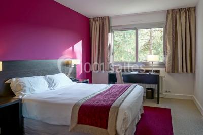 Salle lumineuse avec une grande table dressée pour un repas, décorée de fleurs et entourée de baies vitrées donnant sur un…