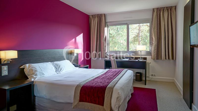 Chambre d'hôtel lumineuse avec un lit double, un bureau près d'une fenêtre et des rideaux beiges.