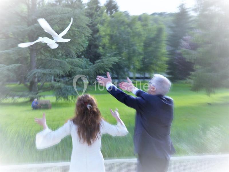 Un couple libère deux colombes blanches dans un parc verdoyant.