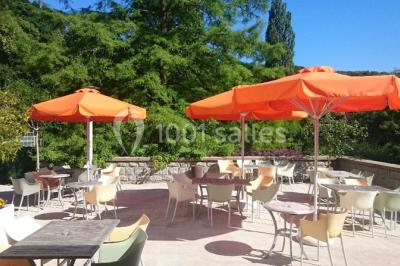 Salle lumineuse avec une grande table dressée pour un repas, décorée de fleurs et entourée de baies vitrées donnant sur un…