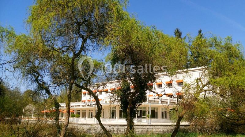 Bâtiment blanc entouré d'arbres avec des branches verdoyantes sous un ciel bleu clair.