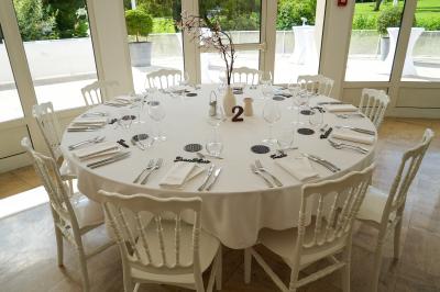 Salle lumineuse avec une grande table dressée pour un repas, décorée de fleurs et entourée de baies vitrées donnant sur un…