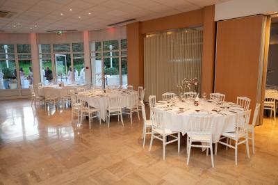 Salle lumineuse avec une grande table dressée pour un repas, décorée de fleurs et entourée de baies vitrées donnant sur un…
