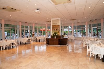 Salle lumineuse avec une grande table dressée pour un repas, décorée de fleurs et entourée de baies vitrées donnant sur un…