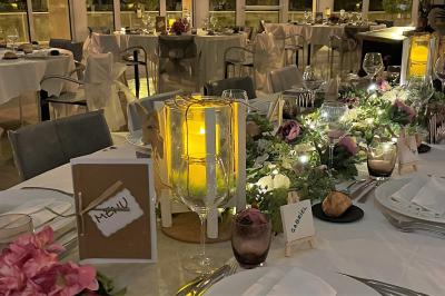 Salle lumineuse avec une grande table dressée pour un repas, décorée de fleurs et entourée de baies vitrées donnant sur un…