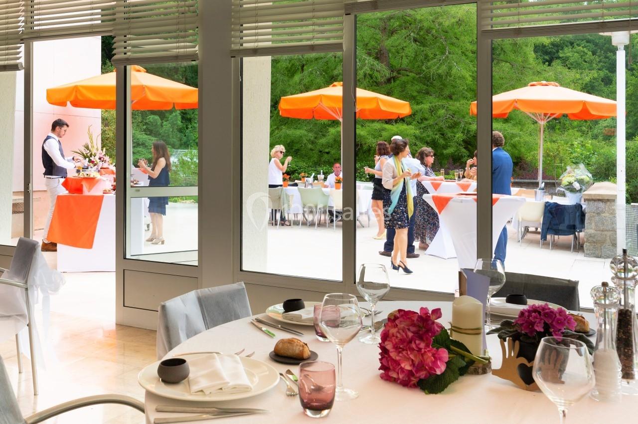 Salle de restaurant lumineuse avec vue sur une terrasse où des personnes discutent sous des parasols orange.