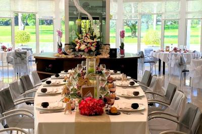 Salle lumineuse avec une grande table dressée pour un repas, décorée de fleurs et entourée de baies vitrées donnant sur un…