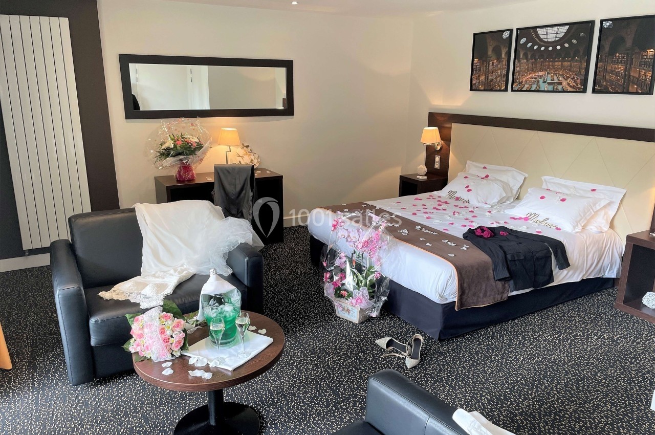 Chambre d'hôtel décorée pour une occasion spéciale, avec lit parsemé de pétales et bouquets de fleurs.