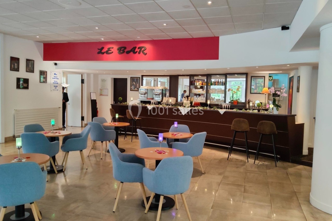Salle de bar moderne avec tables, chaises bleues, comptoir en bois sombre et décoration murale.