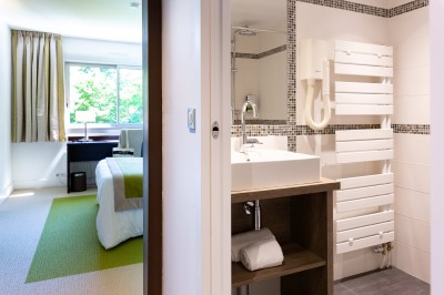 Chambre d'hôtel lumineuse avec un lit double, un bureau près d'une fenêtre et des murs partiellement violets.