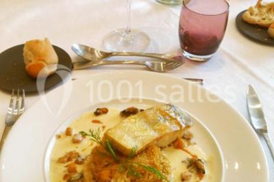 Maison blanche entourée d'arbres, avec terrasse équipée de parasols orange et mobilier de jardin en métal blanc.