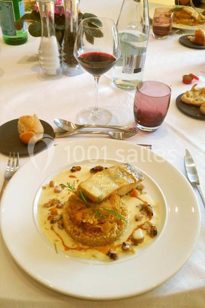 Assiette de poisson grillé avec quinoa, légumes et sauce, servie sur une table dressée avec verre de vin rouge.