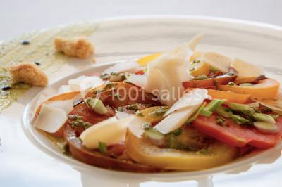 Maison blanche entourée d'arbres, avec terrasse équipée de parasols orange et mobilier de jardin en métal blanc.