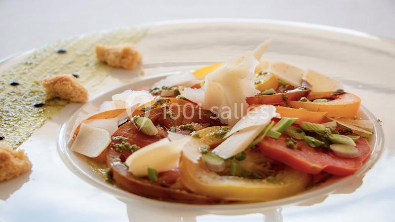 Assiette de tomates colorées garnies de copeaux de fromage, herbes fraîches, croûtons et sauce verte.