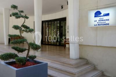 Maison blanche entourée d'arbres, avec terrasse équipée de parasols orange et mobilier de jardin en métal blanc.