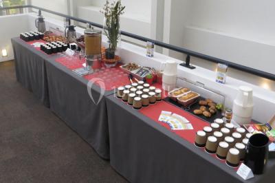 Maison blanche entourée d'arbres, avec terrasse équipée de parasols orange et mobilier de jardin en métal blanc.