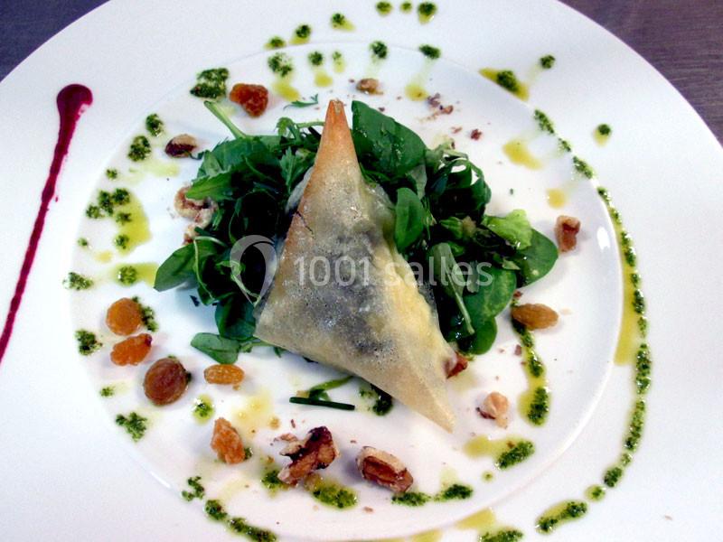 Assiette garnie d'une salade verte, d'un samoussa doré, de raisins secs, de noix et de sauce décorative.