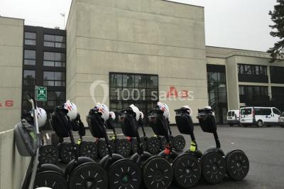 Maison blanche entourée d'arbres, avec terrasse équipée de parasols orange et mobilier de jardin en métal blanc.