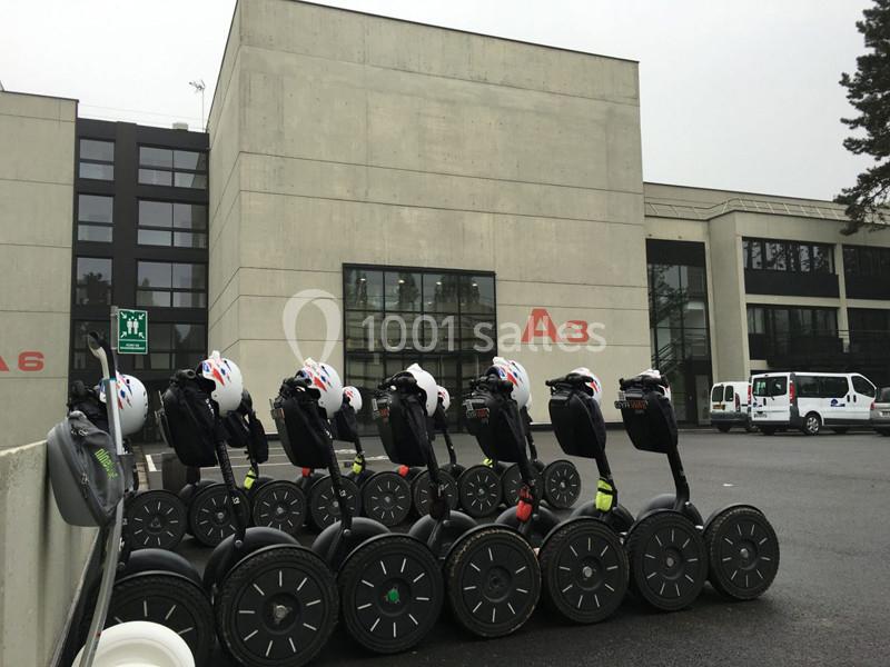 Alignement de gyropodes équipés de casques devant un bâtiment moderne en béton avec des fenêtres vitrées.