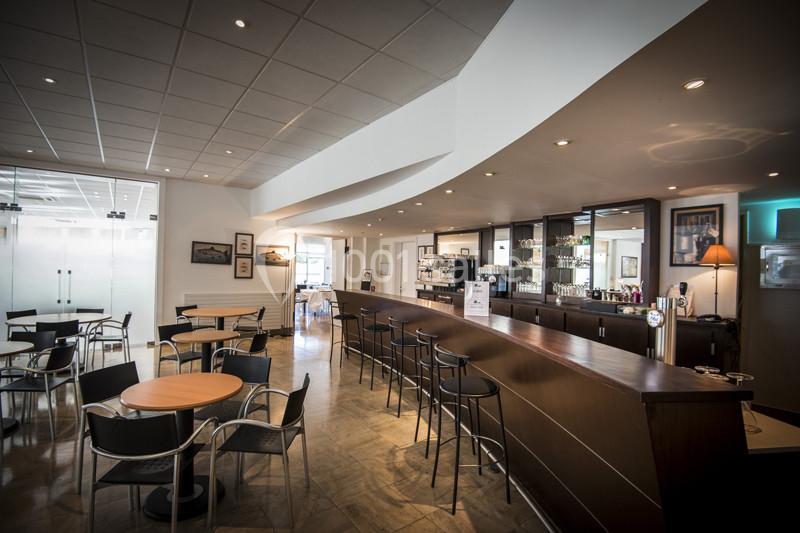 Salle de café moderne avec un bar en bois, des tables rondes, des chaises noires et un éclairage chaleureux.