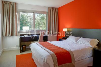 Maison blanche entourée d'arbres, avec terrasse équipée de parasols orange et mobilier de jardin en métal blanc.