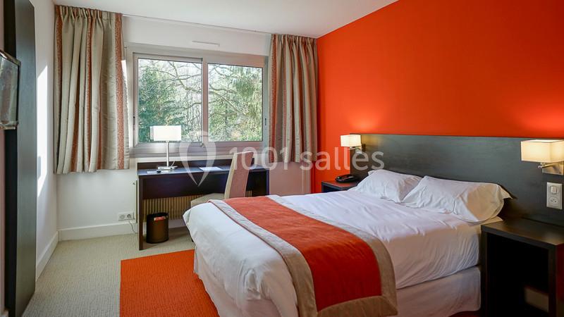 Chambre d'hôtel lumineuse avec un lit double, un bureau près d'une fenêtre et un mur accent orange.