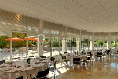 Maison blanche entourée d'arbres, avec terrasse équipée de parasols orange et mobilier de jardin en métal blanc.