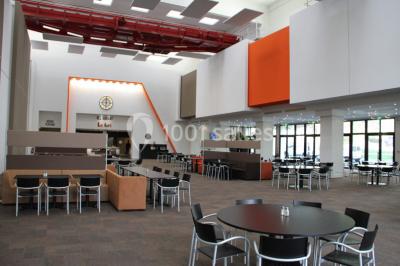 Maison blanche entourée d'arbres, avec terrasse équipée de parasols orange et mobilier de jardin en métal blanc.