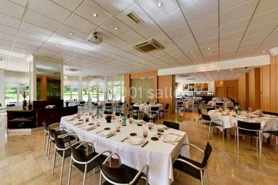 Maison blanche entourée d'arbres, avec terrasse équipée de parasols orange et mobilier de jardin en métal blanc.